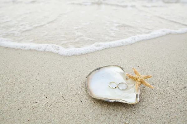 Anneaux de mariage avec coquille et étoile de mer sur la plage de sable blanc — Photo