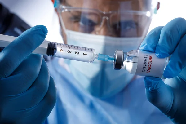医生身穿蓝色制服 戴着防护面具 拿着装有疫苗的注射器 — 图库照片