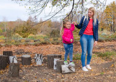 Küçük bir kız parkta yürür ve annesiyle oynar. Altın yapraklı sonbahar manzarası