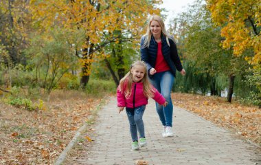 Küçük bir kız parkta yürür ve annesiyle oynar. Altın yapraklı sonbahar manzarası