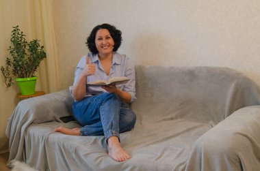 Kanepede oturan bir kadın kitap okuyor.