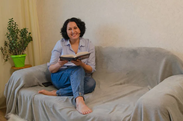A woman reads a book while sitting on the sofa