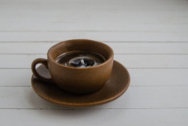Kahverengi fincanda damla olan sade kahve ve beyaz arka planda fincan tabağı.