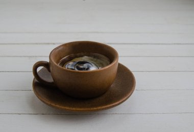 Kahverengi fincanda damla olan sade kahve ve beyaz arka planda fincan tabağı.