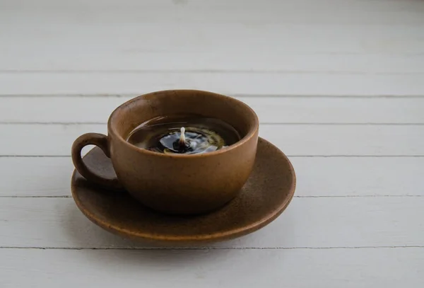 Black coffee with drops in a brown cup and saucer on a white background