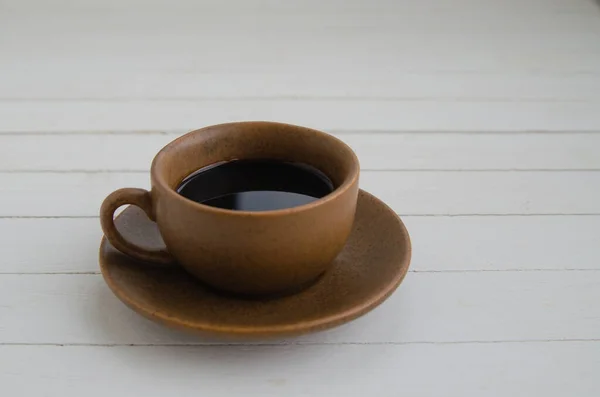 Black coffee with drops in a brown cup and saucer on a white background