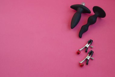 Toys for sex. Nipple clamps and anal dildos on a pink background. clipart