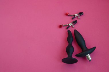 Toys for sex. Nipple clamps and anal dildos on a pink background. clipart