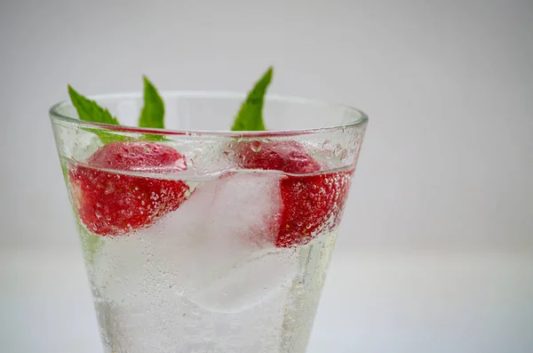 Summer refreshing transparent cocktail with soda, strawberries, mint and ice.