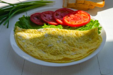 Çırpılmış yumurta, sebzeli beyaz tabakta iki yumurtalı omlet. Hafif ahşap arka planda sağlıklı bir kahvaltı.
