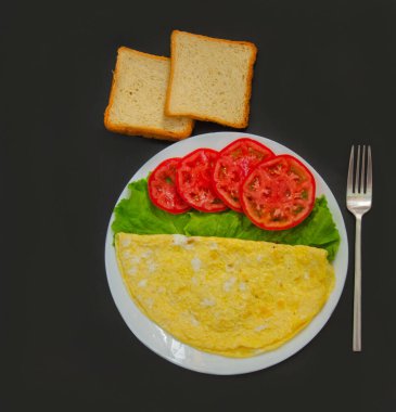 Çırpılmış yumurta, sebzeli beyaz tabakta iki yumurtalı omlet. Sağlıklı kahvaltı ve karanlık bir arka plan.