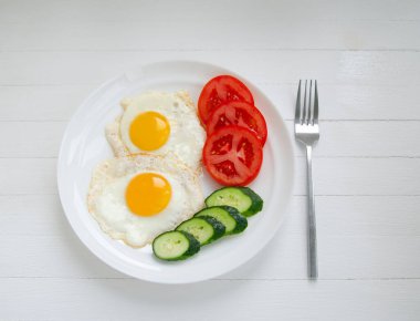 Sebzeli beyaz bir tabakta iki yumurtanın çırpılmış yumurtaları. Beyaz arka planda sağlıklı bir kahvaltı.