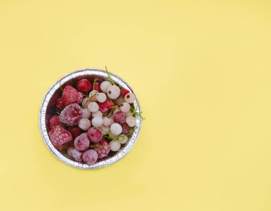 Açık arkaplanda bir folyo tabakasında donmuş ahududu ve kuş üzümü seti.