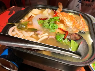 Metal bir yemek tepsisinde yemek haşlayan beyaz Tom Yum. Yengeç, mantar, istiridye, mürekkep balığı, yumurta fasulyesi....
