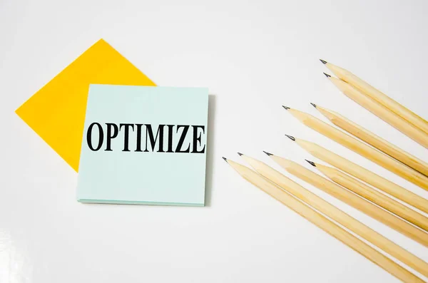 Sarı bir kağıt parçasına yazılmış kelimeleri ve yanında kalemler bulunan beyaz arkaplanı optimize et