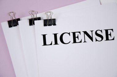 Beyaz kağıt ve pembe arka planda yazılı lisans kelimesi. kelime