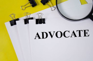 Beyaz kağıda yazılmış ADVOCATE kelimesi ve büyüteçle sarı arkaplan