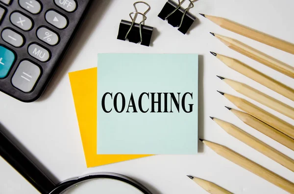 coaching text written on a white notepad with colored pencils and a yellow background. word business concept