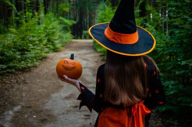 Küçük cadı kız arkası dönük duruyor ve bir balkabağı tutuyor. Cadılar Bayramı konsepti. turuncu