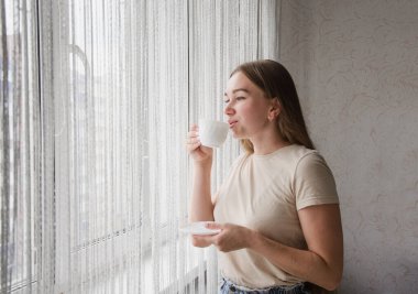 Tatlı kız pencerenin yanında duruyor ve kahve içiyor. Günaydın konsept