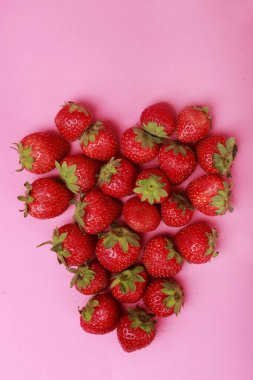 Pembe arka planda kalp şeklinde çilek kompozisyonu.