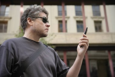 Kafkasyalı bir adam dışarıda cep telefonu ekranına bakıyor.