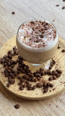 Köpüklü buzlu kahve, kakao tozu ve ahşap yüzeyde kavrulmuş fasulye.