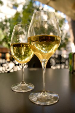 Açık bir kafede siyah bir masada oturan iki beyaz şarap kadehi.