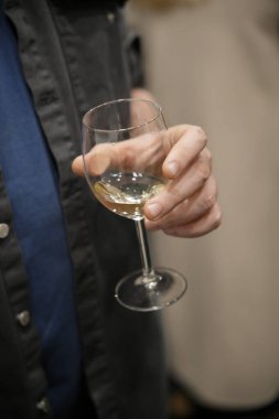 Adam elinde bir bardak beyaz şarap tutuyor, sosyal bir toplantı ya da kutlama öneriyor.