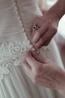 Gelinin özel günü için zarif gelinliğinin düğmelerini ilikleyen eller.