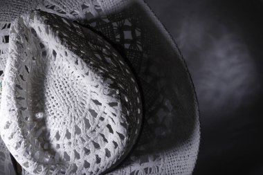 Örgü detaylarıyla el yapımı iki beyaz panama şapkası dramatik ışıklandırmayla aydınlatılmış karanlık bir yüzeyde dinleniyor.