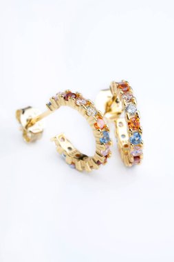 Renkli kristaller içeren bir çift altın halka küpe, canlı ve göz alıcı bir aksesuar oluşturuyor.