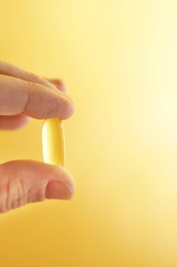 Omega-3 balık yağı kapsülünü canlı sarı bir zemin üzerinde tutan parmaklar.