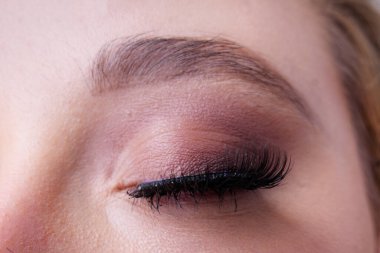 Bir kadının kapalı gözünün yakın çekimi, uzun kirpikleri ve profesyonel makyajı ön plana çıkarıyor.