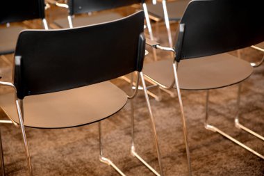Parlak metal bacaklı modern siyah sandalyeler boş bir konferans salonunda, katılımcıların toplantı ya da sunum için gelmelerini bekliyorlar.