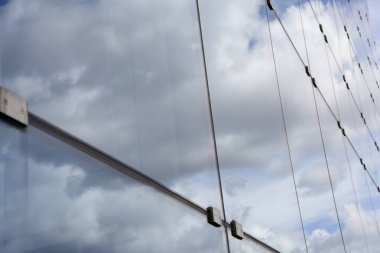 Bulutlu gökyüzünü yansıtan modern bir binanın cam cephesi soyut bir mimari model oluşturuyor.