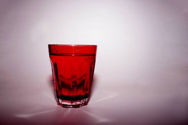 Pembe zemin üzerinde su olan kırmızı cam.