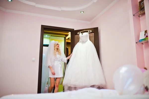 Piękne blond panna młoda patrząc na jej sukni ślubnej — Zdjęcie stockowe