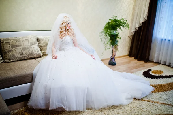 Curly blonde bride sitting and posing on the sofa — Stock Photo, Image