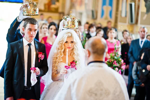 Bruiloft paar in de kerk met kaarsen op handen en kronen op had — Stockfoto