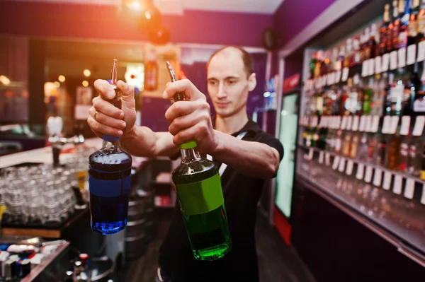 Młody barman trzymając butelki na koktajl w barze — Zdjęcie stockowe
