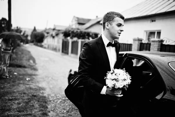 Κομψό νεαρός γαμπρός έξω από το αυτοκίνητο γάμο στη βροχή — Φωτογραφία Αρχείου