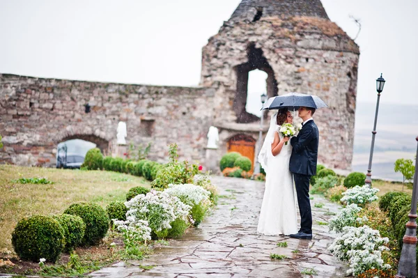Casamento casal andando sob chuva com guarda-chuva torre de fundo — Fotografia de Stock
