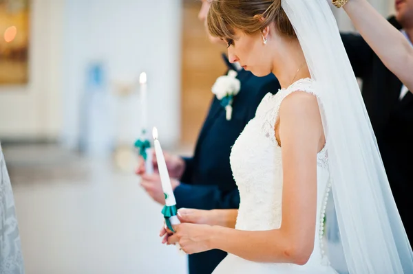 Hochzeitspaar hält Kerzen mit grünen Bändern in der Kirche — Stockfoto