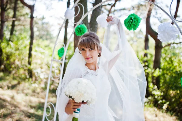 Niedliche Braut mit Brautstrauß in der Nähe von Dekorbogen im Freien — Stockfoto