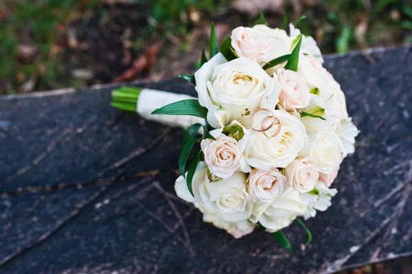 Ramo de boda de rosas con anillos en banco de madera — Foto de Stock