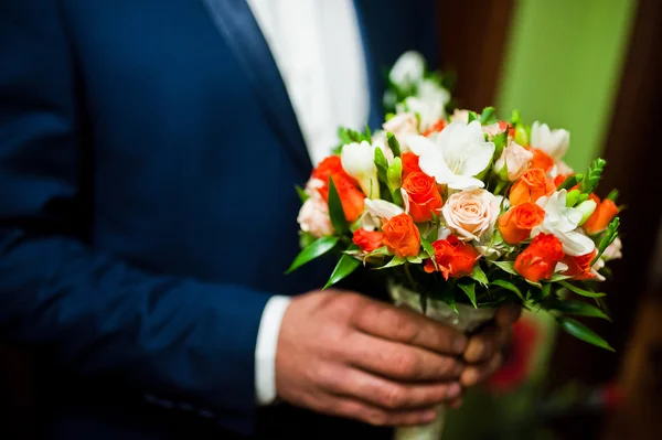 Small wedding bouquet of white and orange roses on hand of groom