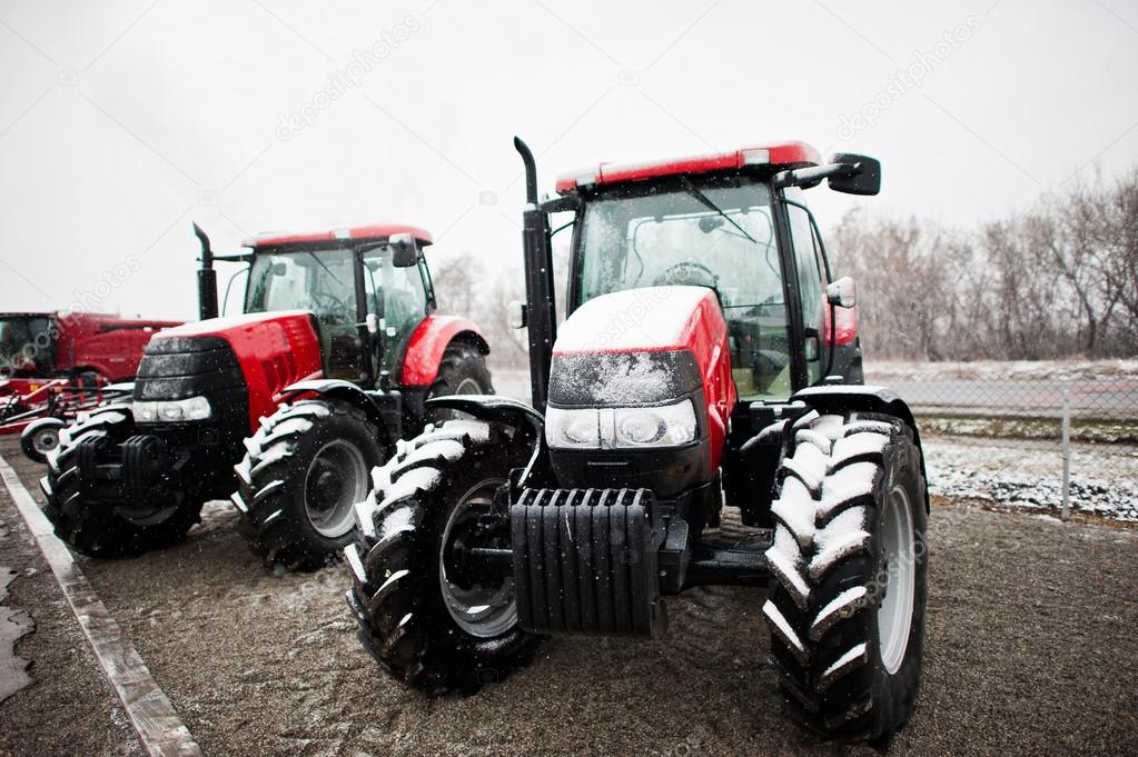 Two new red tractor stay at snowy weather background combine