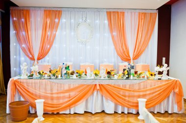 Turuncu perdeleri ve düğün parçası üzerinde yeni evliler, masada sandalye