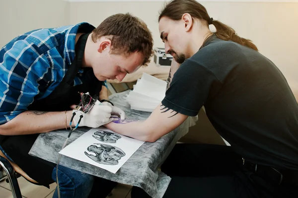 Il maestro del tatuaggio fa il tatuaggio per l'uomo dondolo al salone del tatuaggio — Foto Stock